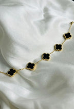 Gold chain bracelet with black clover charms displayed on white silk fabric