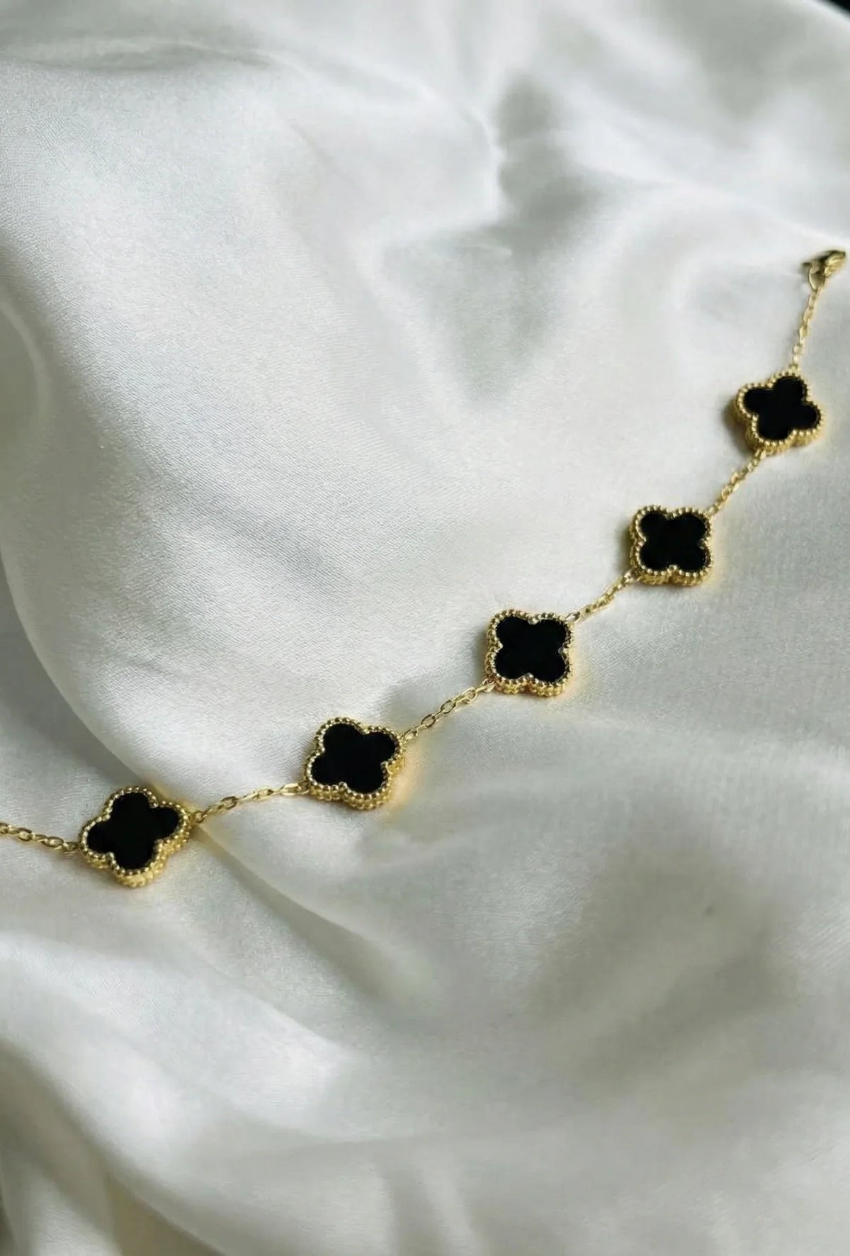 Gold chain bracelet with black clover charms displayed on white silk fabric