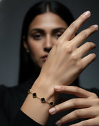 Woman wearing a gold bracelet with black clover charms, hand raised, on dark background