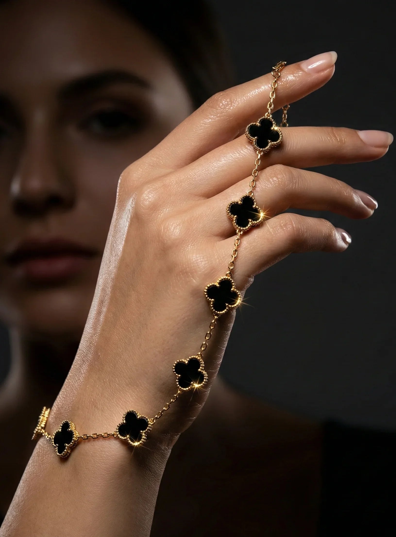 Hand modeling gold bracelet with black clover-shaped charms on dark background