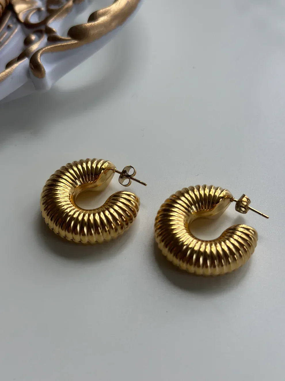 Pair of chunky gold ribbed hoop earrings on white surface