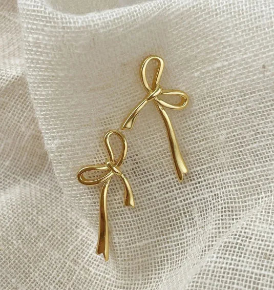 Gold bow knot earrings displayed on textured beige fabric