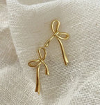 Gold bow knot earrings displayed on textured beige fabric