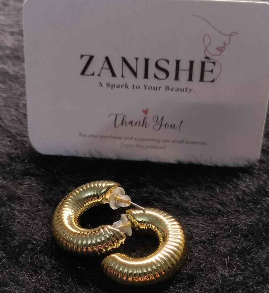 Textured gold hoop earrings with card on black surface